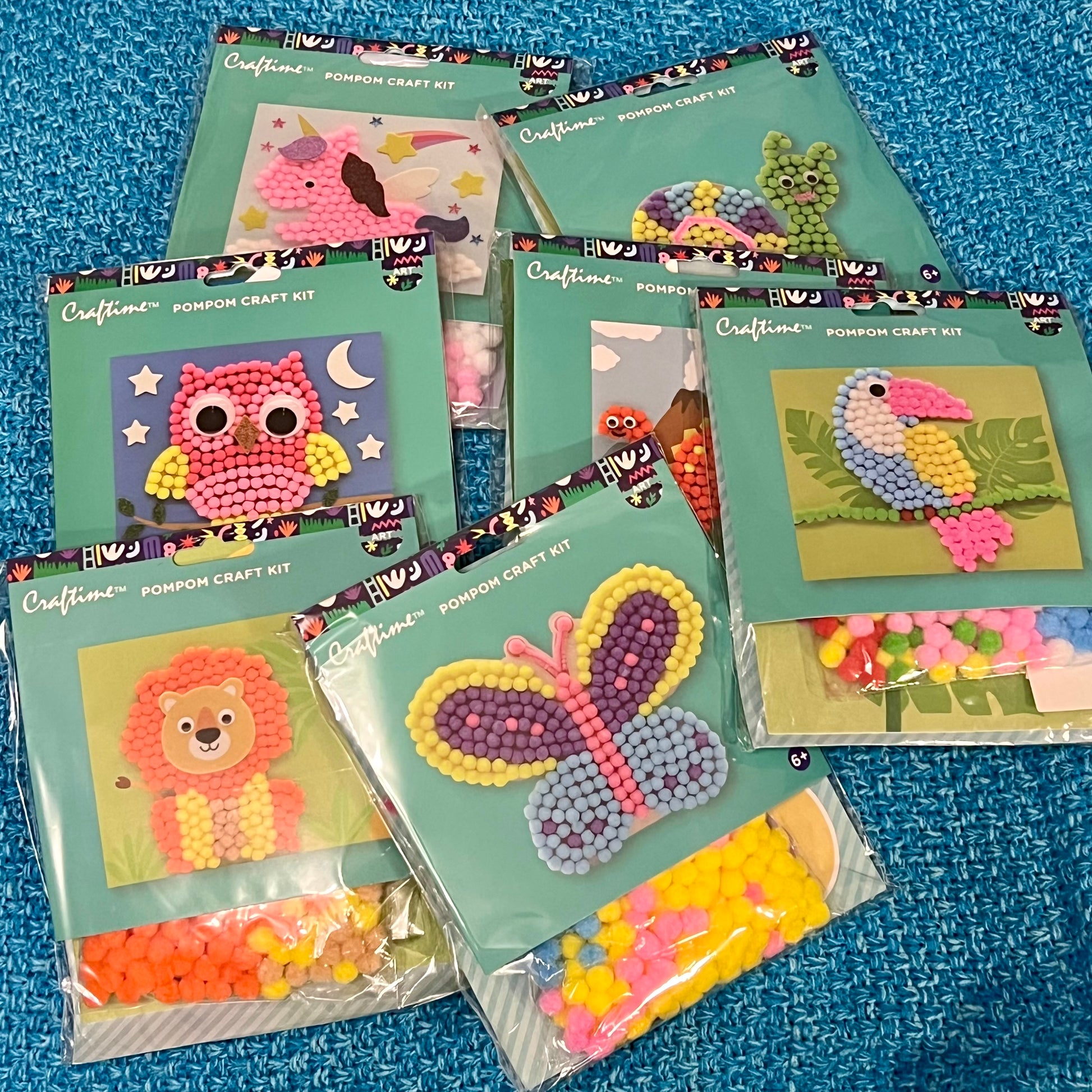 Collection of Craftime pom-pom craft kits on a blue textured background